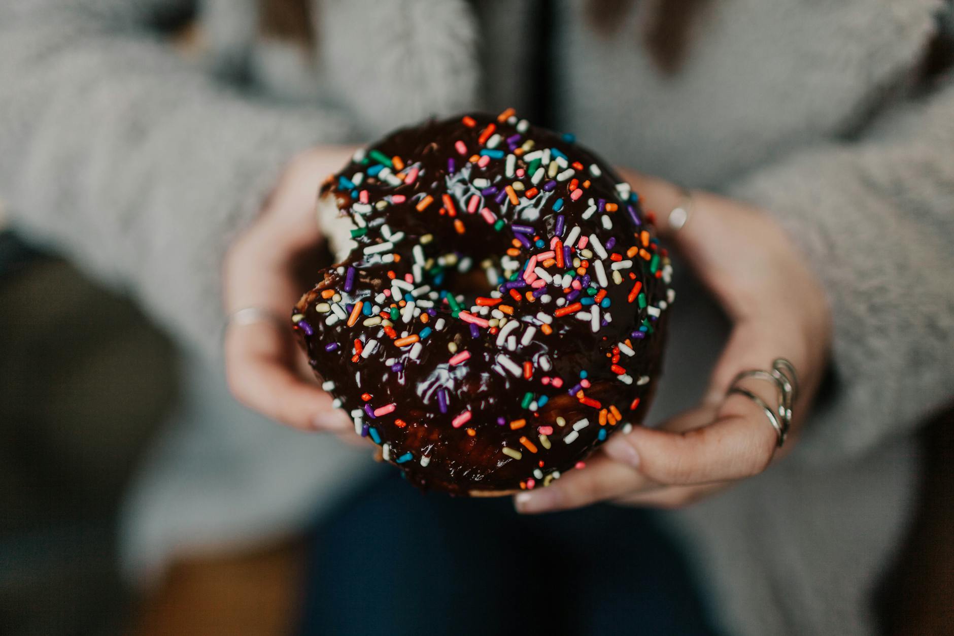 Dłonie trzymają czekoladowego pączka z kolorową posypką