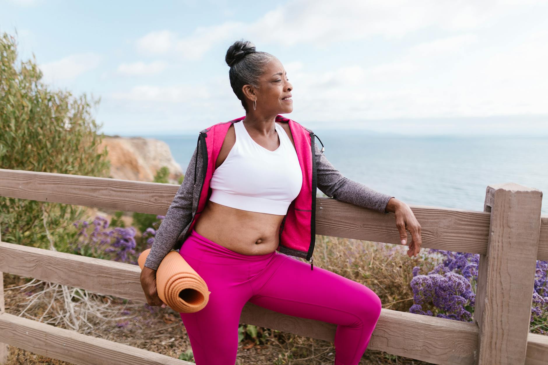 Starsza kobieta w stroju sportowym z matą do jogi nad morzem