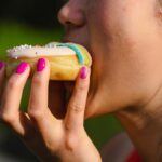 Kobieta z pomalowanymi paznokciami gryzie kolorowego pączka z posypką