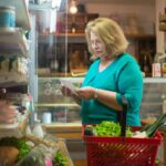 Starsza kobieta z listą zakupów i koszykiem w supermarkecie