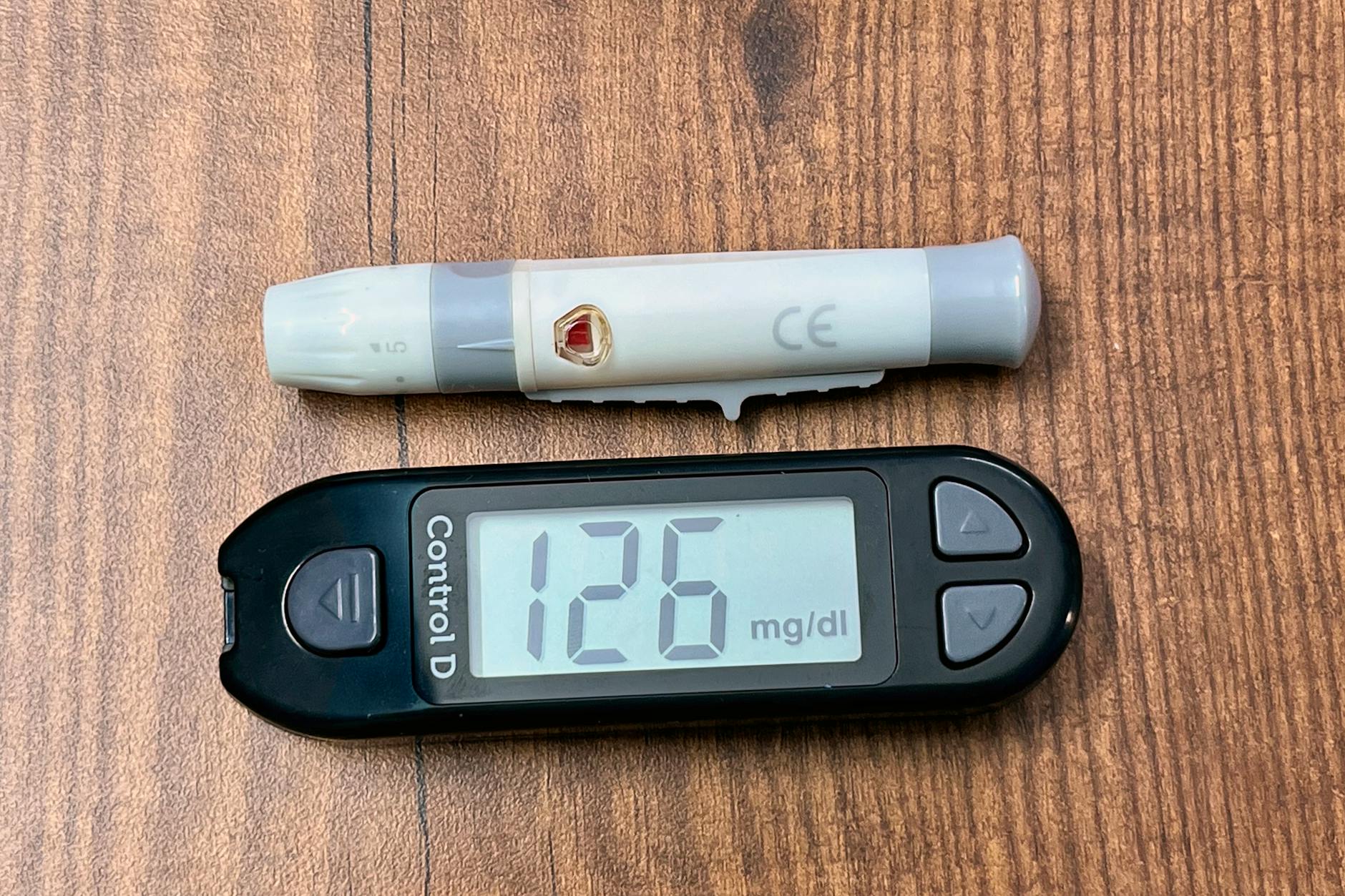 Glucometr pokazujący wynik 126 mg/dL i nakłuwacz na drewnianym blacie