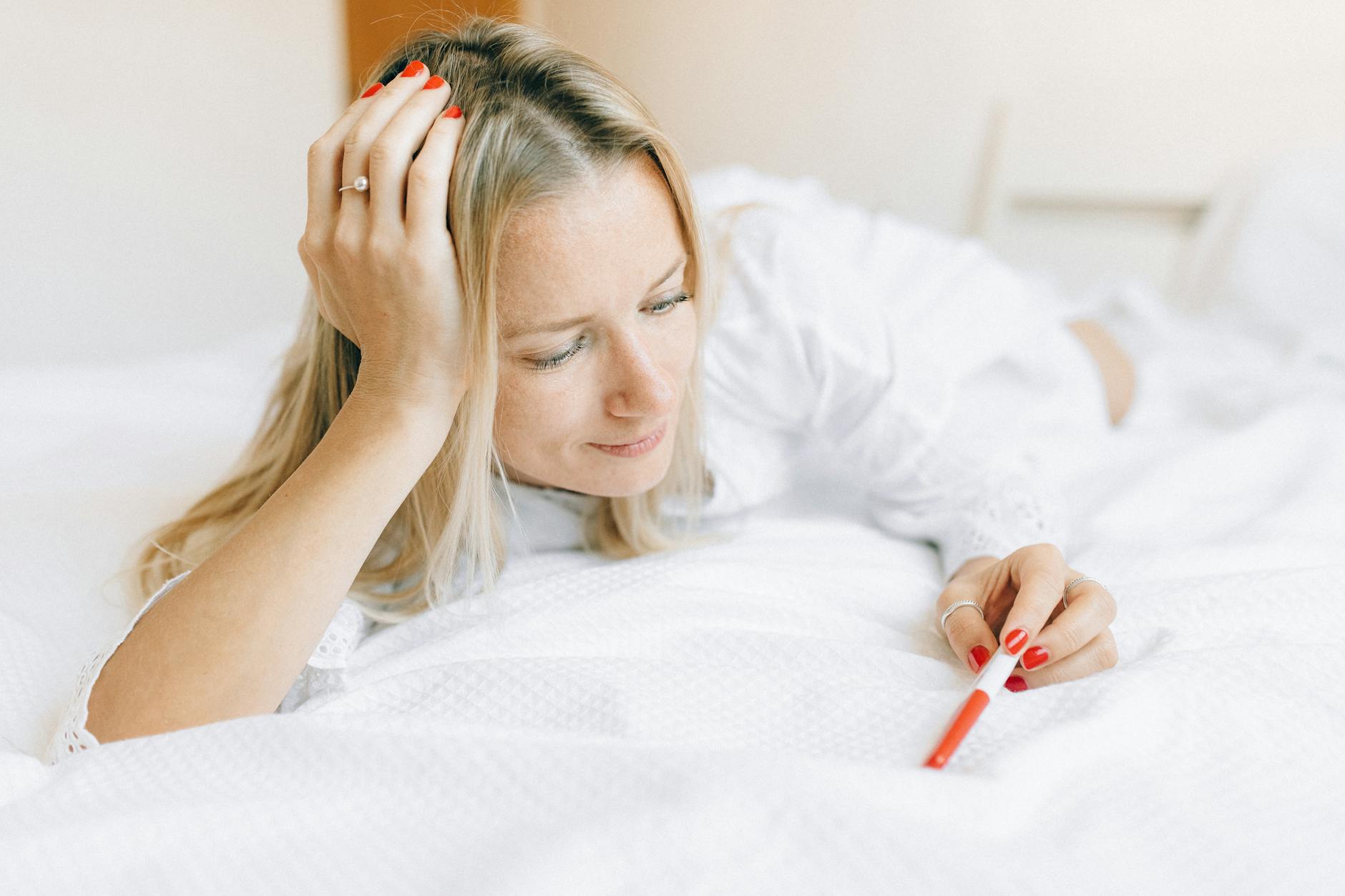 Kobieta leżąca w łóżku w skupieniu patrzy na test ciążowy