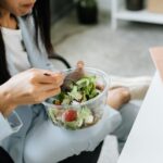 Kobieta przy biurku w pracy je sałatkę warzywną na szybki, zdrowy lunch