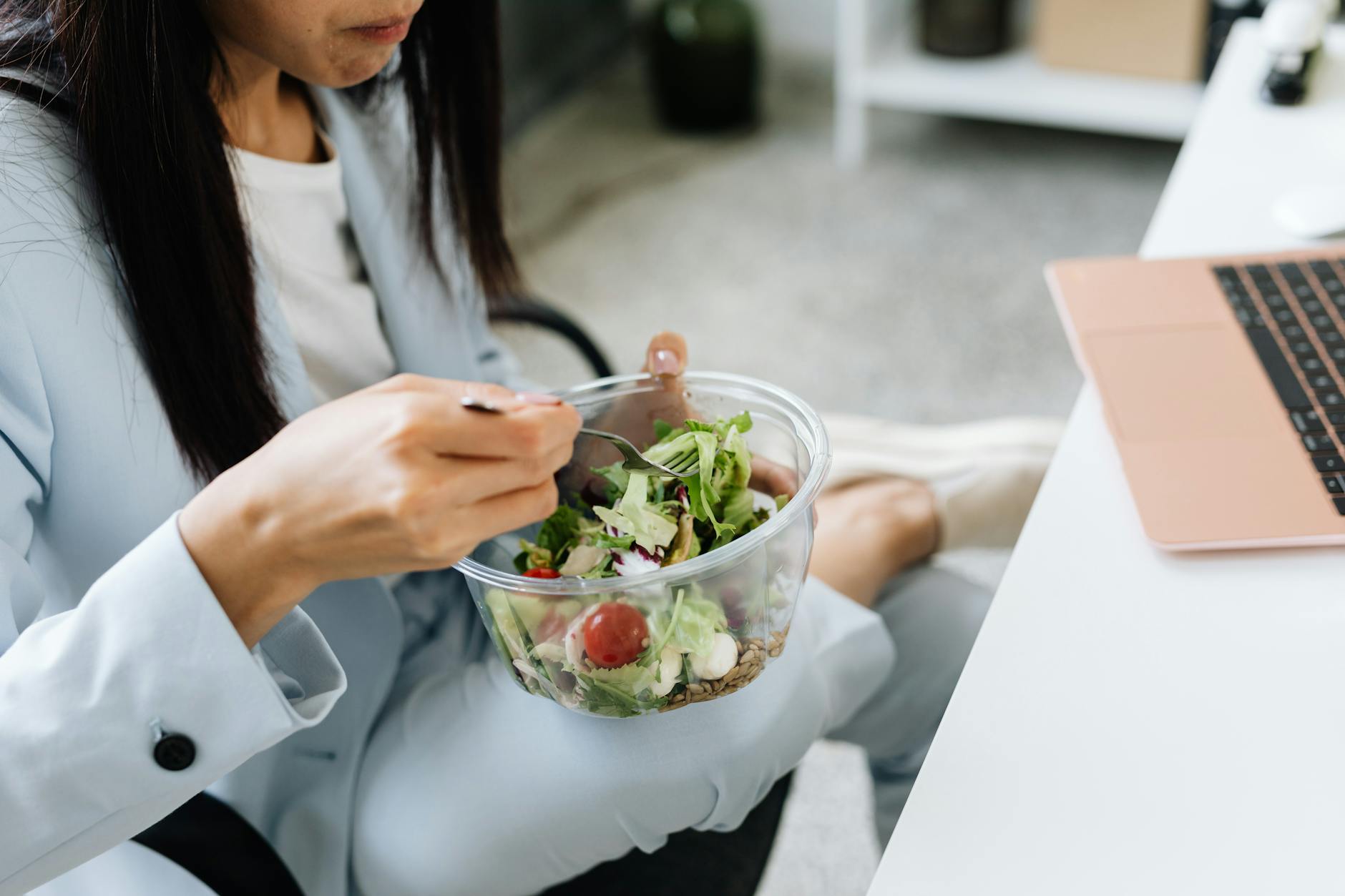 Kobieta przy biurku w pracy je sałatkę warzywną na szybki, zdrowy lunch Kobieta przy biurku w pracy je sałatkę warzywną na szybki, zdrowy lunch