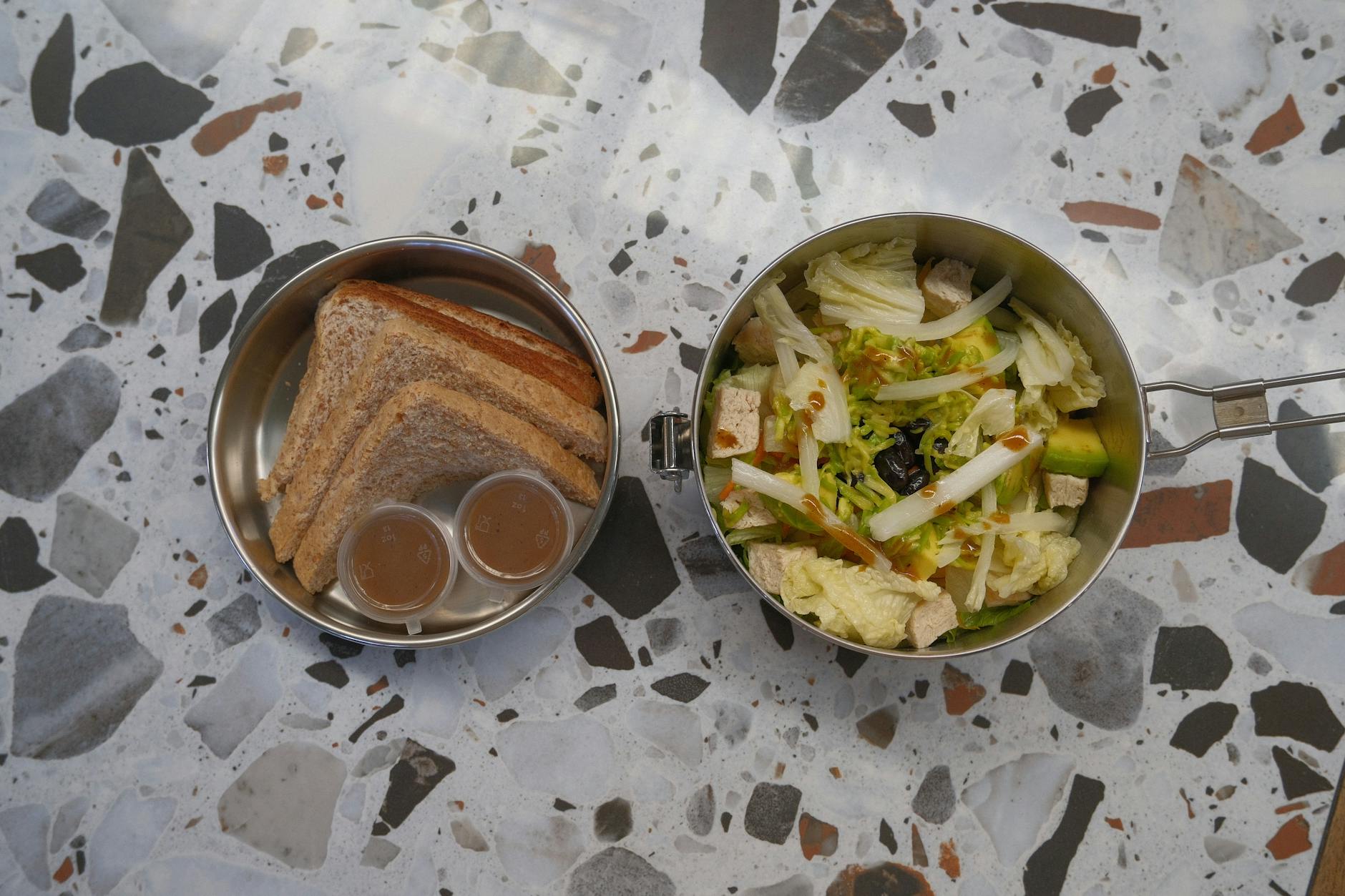 Lunchbox z kanapkami, sałatką i sosem na jasnym blacie